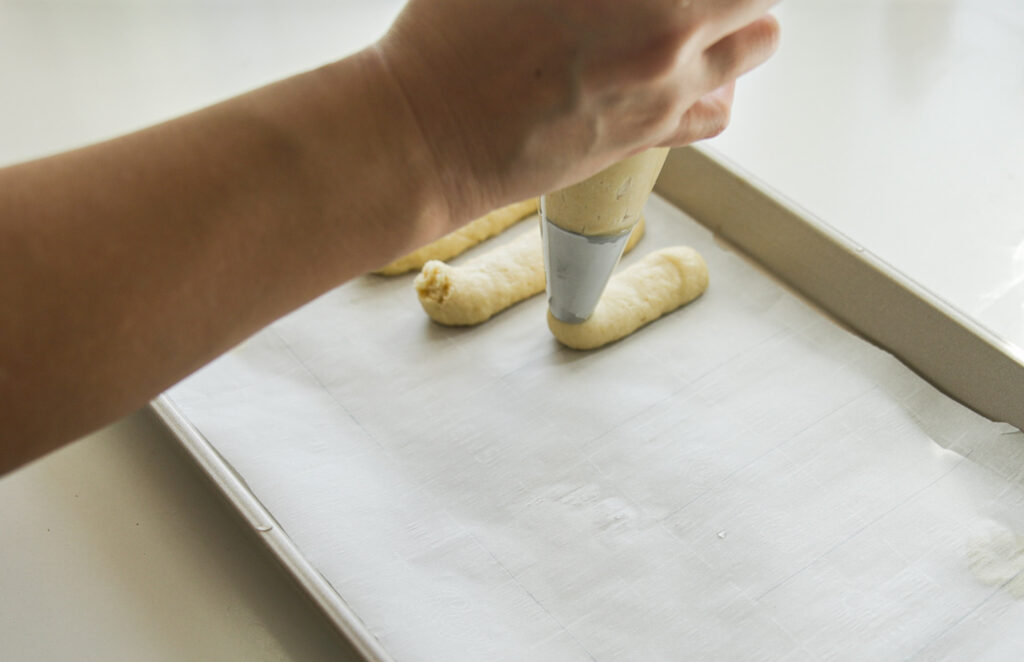 piping ladyfinger dough onto baking sheet with parchment paper